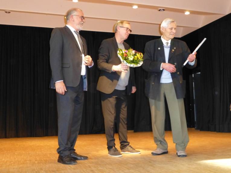 Drei Herren stehen nebeneinander, einer hält einen Blumenstrauß, der den Ehrenpreis 2022 erhalten hat